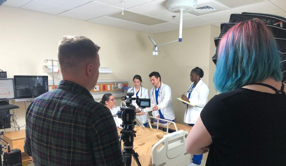 Two individuals filming nursing students in discussion with a patient.